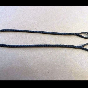 May include: A black string with two loops at the ends. The string is lying flat on a brown surface.