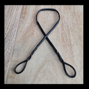 Puede incluir: Cordón trenzado negro con dos bucles en los extremos. El cordón está atado en un nudo de ocho.