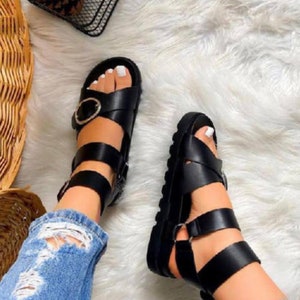 May include: Black leather sandals with multiple straps and a buckle closure. The sandals have a chunky platform sole.
