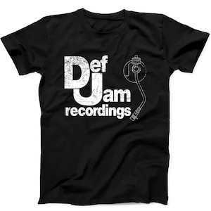 May include: A black short-sleeved t-shirt featuring a white distressed graphic print on the chest. The design displays the text Def Jam recordings in a bold, weathered font, accompanied by a line-art illustration of a turntable tonearm.
