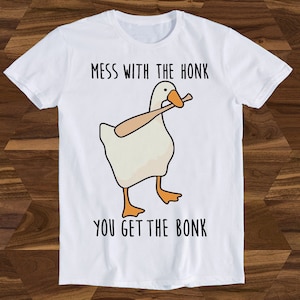 Puede incluir: Camiseta blanca con un dibujo animado de un ganso sosteniendo un bate de béisbol. El texto "MESS WITH THE HONK YOU GET THE BONK" está impreso en la camiseta.