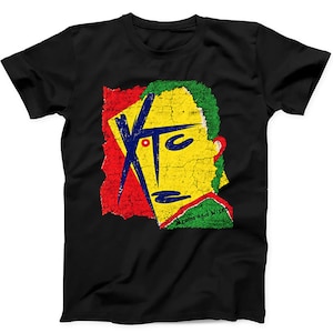 May include: A black short-sleeve t-shirt featuring a graphic print with a distressed, cracked texture. The design displays the letters XTC in blue, set against a yellow, red, and green background. The text Drums and Wires is visible.
