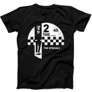 Puede incluir: Una camiseta negra de manga corta con un estampado gráfico blanco desgastado. El diseño incluye la silueta de una persona con traje y sombrero, un patrón de cuadros y el texto 2 TONE RECORDS 45 THE SPECIALS en una disposición circular.