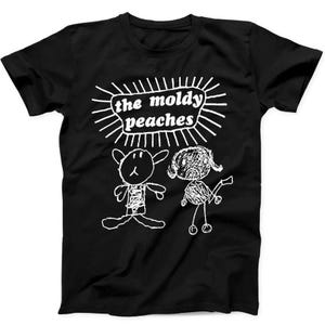 May include: A black short-sleeved t-shirt featuring a white graphic print. The design includes the text "the moldy peaches" inside a sunburst shape, positioned above two hand-drawn style figures, one resembling a rabbit and the other a person.