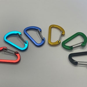 May include: Six colorful metal carabiners in a rainbow pattern. The carabiners are arranged in a semi-circle with the red one at the bottom and the black one at the top.