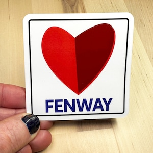 May include: A square sticker with a white background, black border, and a split heart design in red and dark red. The word "FENWAY" is printed in blue block letters below the heart.