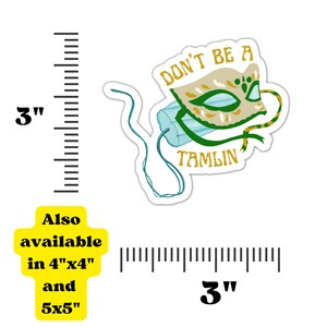 Może przedstawiać: Naklejka z motywem maski i napisem "DON'T BE A TAMLIN". Maska jest beżowa z zielonymi i złotymi detalami. Naklejka ma około 7,6 cm i jest r&oacute;wnież dostępna w rozmiarach 10,2 cm x 10,2 cm i 12,7 cm x 12,7 cm. Z maski wychodzi turkusowy sznurek.