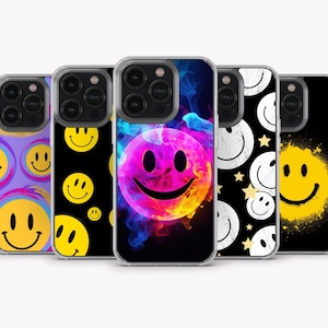 May include: Five phone cases with smiley face designs. The cases display a variety of colours, including purple, black, and yellow. One case has a vibrant, colourful smiley face against a dark background.