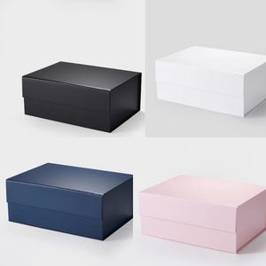 May include: Four rectangular gift boxes in different colors: black, white, navy blue, and light pink. Each box has a smooth, matte finish and a matching lid. The boxes are arranged in a square formation against a plain white background.