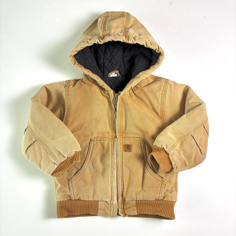 May include: A tan hooded jacket with a black quilted lining. The jacket features a full zipper, two front pockets, and ribbed cuffs and hem. A small logo patch is on the front pocket.