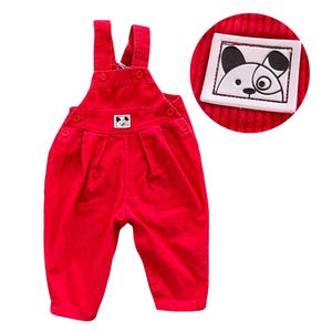 May include: Red corduroy overalls with adjustable straps and a small white patch featuring a black and white cartoon dog on the front.