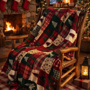 May include: A patchwork throw blanket featuring a festive pattern of red and green plaid squares, cream-colored squares with dark green pine tree silhouettes, and small snowflake motifs, draped over a wooden rocking chair.
