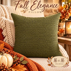 May include: A square olive green knit cushion with a textured surface. The image includes the text Fall Elegance PILLOW and a label indicating the size is 16 x 16 inches. The cushion is displayed in a setting with autumn-themed decor.
