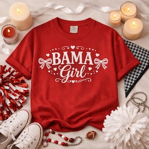 May include: A red t-shirt with the text "BAMA Girl" in white script and decorative elements. The shirt is surrounded by candles, a pom-pom, a football, and white sneakers.