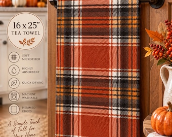 May include: A rectangular tea towel measuring 16 x 25 inches featuring a plaid pattern in shades of burnt orange, dark brown, white, and black. The towel hangs from a black metal bar and has a soft, absorbent texture with finished edges.