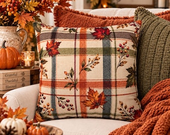 May include: A square throw pillow featuring a cream-colored base with a plaid pattern in shades of orange, green, and dark blue. The design is decorated with printed autumn maple leaves and clusters of red berries scattered across the fabric surface.