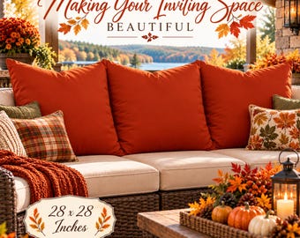 May include: Three large solid burnt orange square throw pillows on a beige outdoor sofa, accompanied by smaller plaid and leaf-patterned accent pillows, a knit throw, and a tray with pumpkins, measuring 28 x 28 inches.