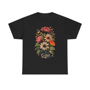 Peut inclure: T-shirt noir avec un motif floral. Le motif comprend des fleurs roses, oranges et blanches, et des feuilles vertes. Les mots "Grow with Grace" sont écrits en cursive sous les fleurs.