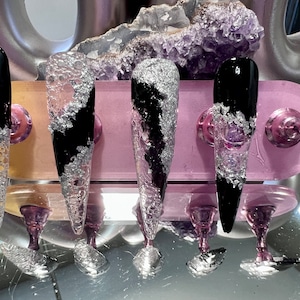 Può includere: Cinque punte per unghie lunghe, nere e argentate con una finitura testurizzata e spumosa. Le punte sono esposte su un supporto rosa e bianco.