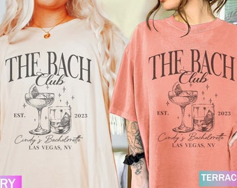 May include: Ivory and terracotta-colored t-shirts with a graphic design. The design includes the text "THE BACH Club" above an illustration of a cocktail and a rocks glass. Below the illustration is "EST. 2023" and "Cindy's Bachelorette, LAS VEGAS, NV."