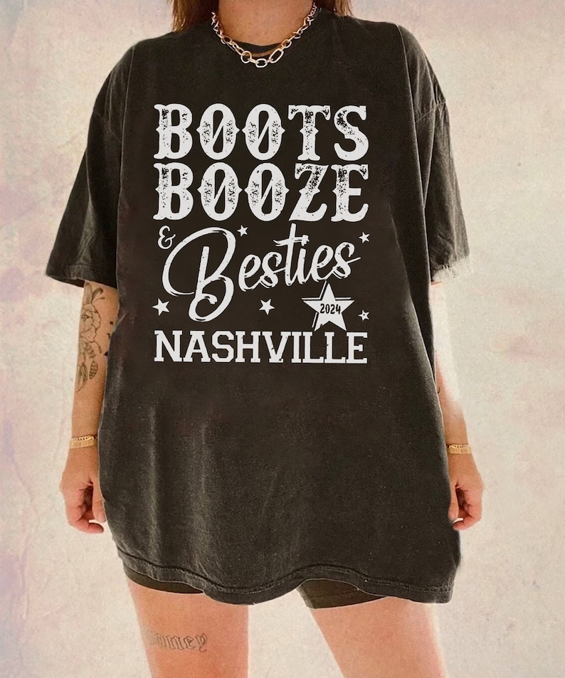 Może przedstawiać: Czarny t-shirt z białym napisem "Boots, Booze & Besties Nashville 2024". Tekst jest ułożony w stos z gwiazdami i gwiazdą z rokiem 2024. Koszulka ma wygląd vintage.