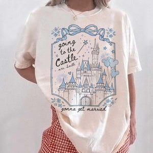 May include: Cream t-shirt with a blue and white castle graphic. The text reads "going to the Castle mrs. Smith gonna get married". The design includes a bow, flowers, stars, and a magic wand.