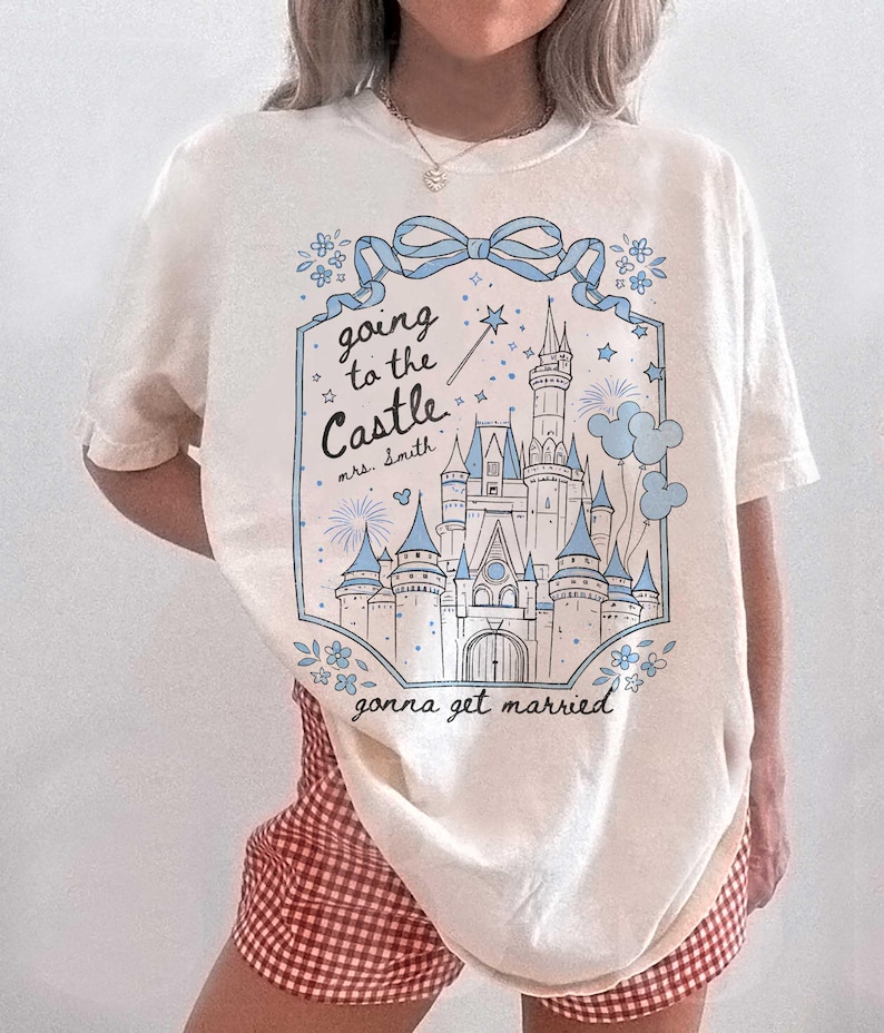May include: Cream t-shirt with a blue and white castle graphic. The text reads "going to the Castle mrs. Smith gonna get married". The design includes a bow, flowers, stars, and a magic wand.