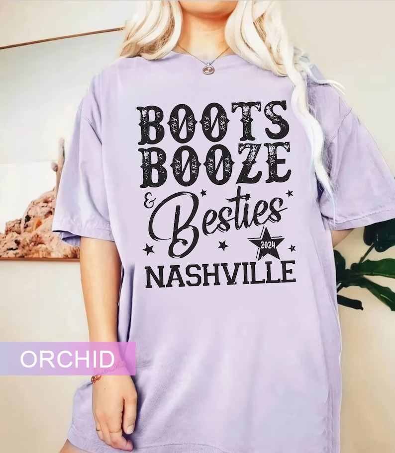 Może przedstawiać: Fioletowa koszulka z czarnym napisem "Boots, Booze & Besties Nashville 2024". Projekt zawiera gwiazdy i gwiazdę z rokiem 2024. Koszulka ma luźny kr&oacute;j.