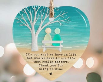 May include: Heart-shaped wooden ornament with a beach scene, a tree, and two figures on a bench. The ornament has the text "It's not what we have in life but who we have in our life that really matters. Thank you for being in mine."