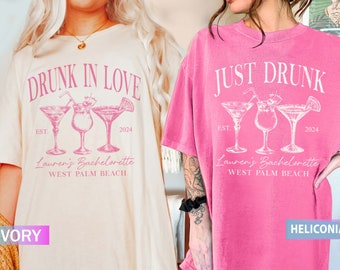 May include: Two white t-shirts with pink text and graphics. The left shirt says "Drunk in Love" with three cocktail glasses and the text "Est. 2024" and "Lauren's Bachelorette West Palm Beach". The right shirt says "Just Drunk" with three cocktail glasses and the text "Est. 2024" and "Lauren's Bachelorette West Palm Beach". The left shirt is ivory and the right shirt is pink.