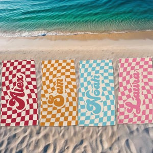 May include: Four beach towels with checkered patterns in red, orange, blue, and pink. Each towel has a name in a retro font: Alex, Sam, Noah, and Laura.