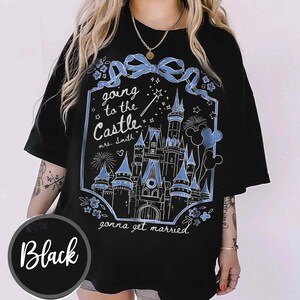 May include: Black t-shirt featuring a light blue castle graphic, fireworks, and Mickey Mouse balloons. Text says "going to the Castle mrs. Smith gonna get married". The shirt has a round neck and short sleeves.