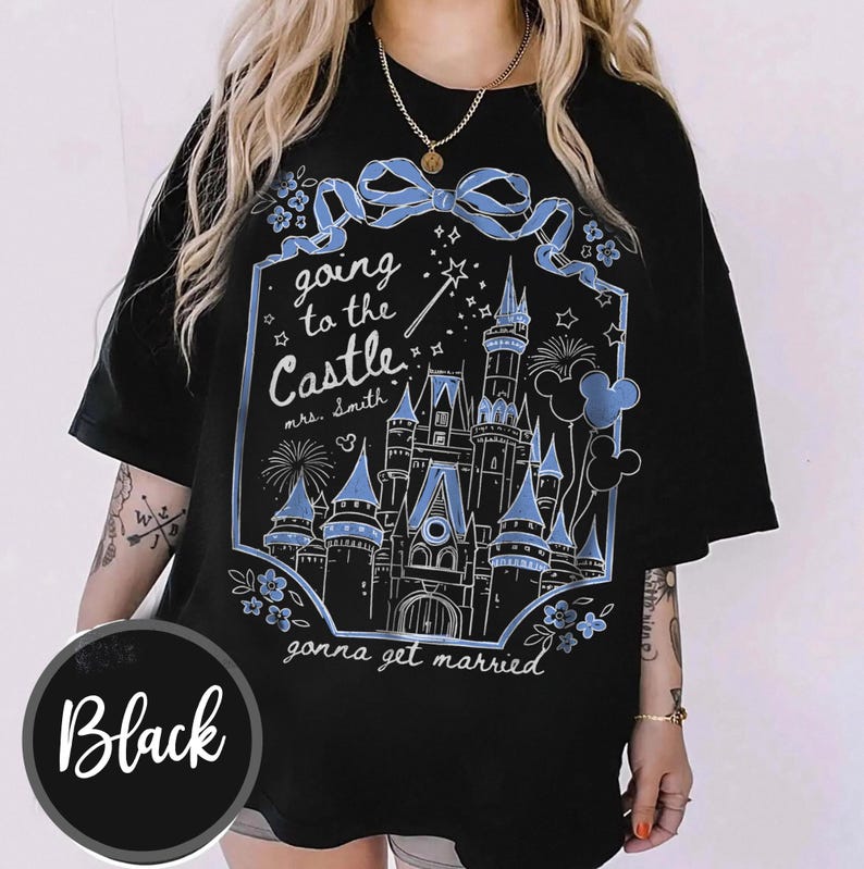 May include: Black t-shirt featuring a light blue castle graphic, fireworks, and Mickey Mouse balloons. Text says "going to the Castle mrs. Smith gonna get married". The shirt has a round neck and short sleeves.