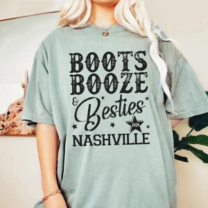 Może przedstawiać: Szałwiowa koszulka z napisem "Boots, Booze & Besties Nashville 2024" w czarnym, postarzanym kroju. Projekt zawiera gwiazdy i grafikę gwiazdy. Koszulka ma kr&oacute;tkie rękawy i luźny kr&oacute;j.