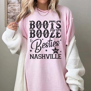 Może przedstawiać: Jasnor&oacute;żowa koszulka z czarnym napisem "BOOTS BOOZE & Besties NASHVILLE 2024". Koszulka ma luźny kr&oacute;j i jest noszona przez osobę. Słowo "BLOSSOM" jest wydrukowane w prawym g&oacute;rnym rogu.