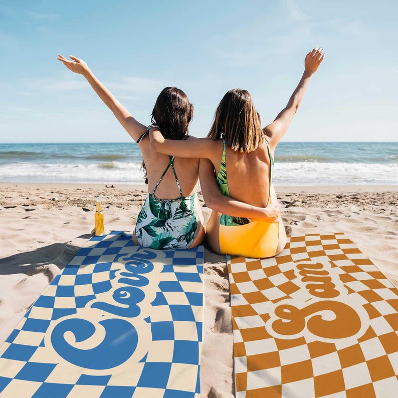 May include: Two people are sitting on beach towels with checkered patterns. The towels have the words "Clover" and "Cream" printed on them in a retro font.