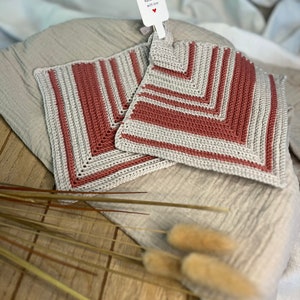 Könnte beinhalten: Zwei gehäkelte Topflappen mit einem gestreiften Muster in Beige und Rosa. Die Topflappen sind handgefertigt und haben ein Etikett mit der Aufschrift "Handgefertigt mit Liebe".