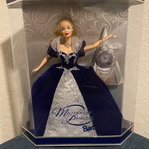 May include: A blue and silver Millennium Princess Barbie doll in a clear plastic display box. The box has a blue and silver trim and the words "Special Millennium Edition" on the top. The doll is wearing a blue velvet gown with silver sequins and a silver tiara. The doll is holding a silver orb with the words "Millennium Keepsake" on it.