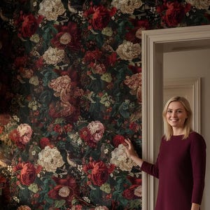 May include: A kitchen with dark green cabinets and a black countertop. The walls are covered in floral wallpaper with red and white flowers. A woman in a burgundy dress stands in the doorway. A decorative pillow with a floral pattern sits on a bench.