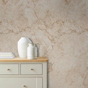 Op de afbeelding: Een witte commode met vier lades en een houten blad. Een witte vaas en een witte kan met een bloemenpatroon staan op de commode. Een bruine rieten mand met witte handdoeken staat op de vloer voor de commode. De muur achter de commode is een beige marmerbehang.