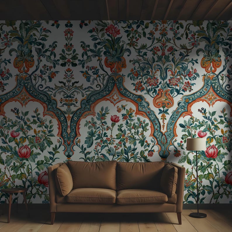 Op de afbeelding: Een kamer met een bruine bank, een bijzettafel en een vloerlamp. De blikvanger is een muur bedekt met bloemenbehang met een witte achtergrond en sierlijke teal, oranje en groene patronen. De kamer heeft een warme, uitnodigende sfeer.