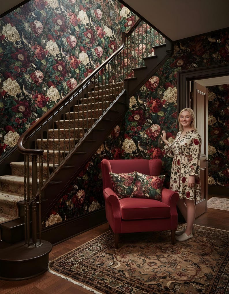 May include: A red armchair with floral pillows sits on a patterned rug in front of a staircase. The walls are covered in dark floral wallpaper. A person wearing a floral dress stands near the door.