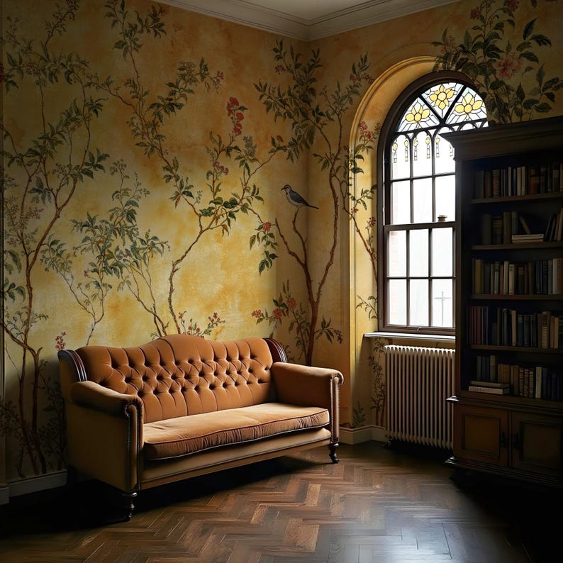 May include: A brown velvet tufted sofa sits in a room with a yellow and brown floral wallpaper, a large arched window with stained glass, and a dark wood bookcase filled with books.