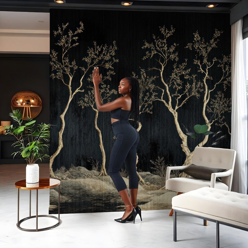May include: A black and gold wallpaper mural with a stylized design of trees with gold leaves. A person is standing in front of the mural, wearing black pants and a black top.
