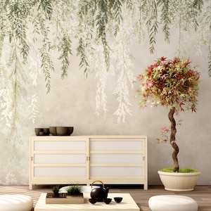 May include: A serene interior scene featuring a low, light wood coffee table with a black teapot and cups. A bonsai tree with red and green leaves sits in a white pot. A light wood cabinet with sliding doors is in the background, with a wall mural of hanging leaves.
