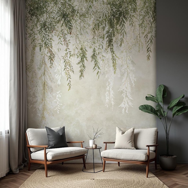 May include: A serene interior scene featuring two armchairs with light-colored upholstery and wooden frames. A small side table sits between them. The backdrop is a wall mural with a botanical design of hanging green and white leaves, creating a calming atmosphere.
