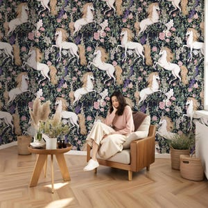 May include: A dark blue wallpaper with a repeating pattern of white unicorns and pink flowers. A woman is sitting in a chair in front of the wallpaper.