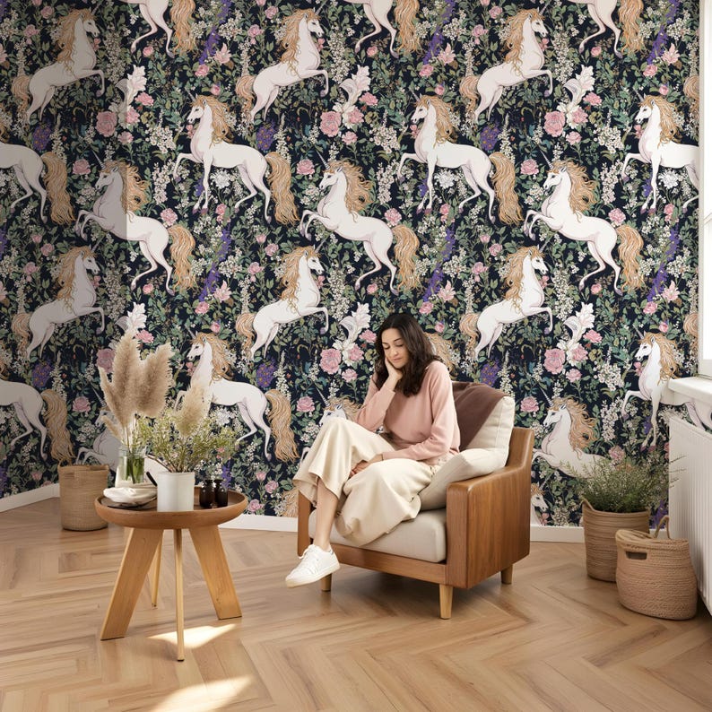 May include: A dark blue wallpaper with a repeating pattern of white unicorns and pink flowers. A woman is sitting in a chair in front of the wallpaper.