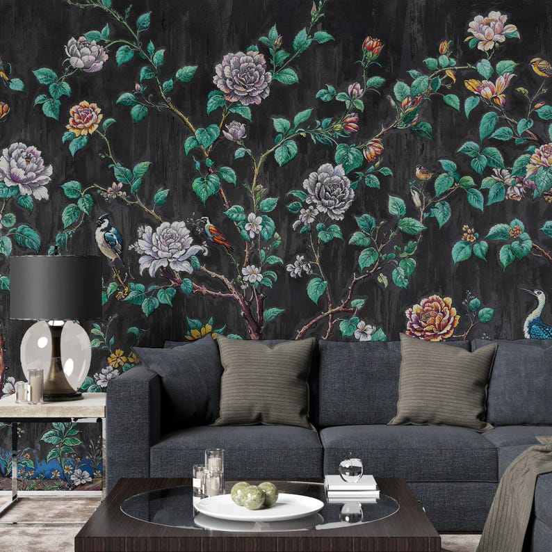 May include: A dark floral wallpaper with large, colourful flowers and green leaves against a black background. The design includes birds perched on branches. A dark grey sofa with cushions and a coffee table are in front of the wallpaper.