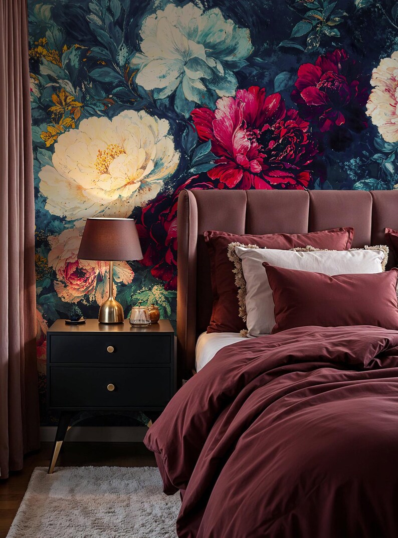 May include: A bedroom scene featuring a floral wallpaper with large white and red flowers. A burgundy bed with matching bedding and pillows is on the right. A black nightstand with a gold lamp and a small rug complete the scene.